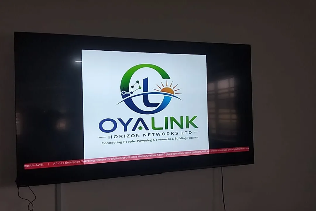 An OyaLink screen live on-site in Uyo — a wall-mounted display showing the OyaLink brand and the AdOS ticker.